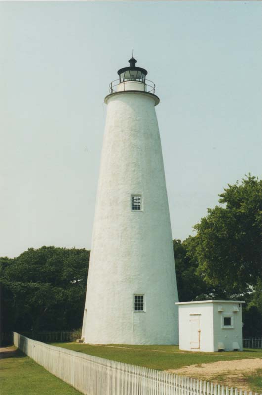 lighthouse with white tower with two small windows and white picket fence in foreground